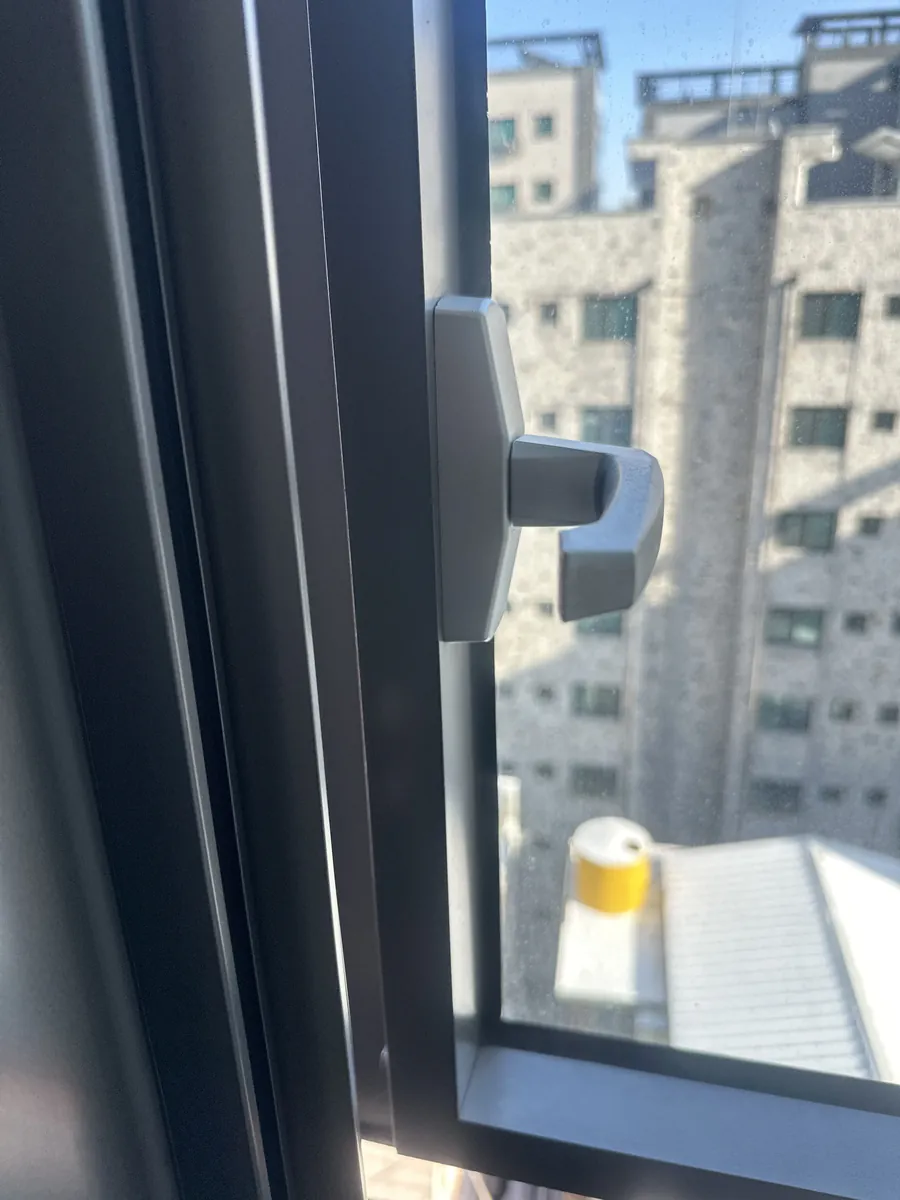 빌딩 창문 손잡이 레버 클로즈업, 도로변이 보이는 고층 창가에서 손잡이 상태를 확인하는 모습